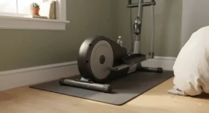 Close-up view of a compact home elliptical machine resting on a protective mat on a bedroom hardwood floor.