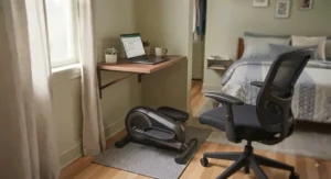 A portable mini elliptical machine positioned near a bedroom desk for convenient exercise.