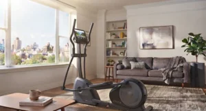 A quiet elliptical machine placed next to a comfortable sofa in an apartment living room.